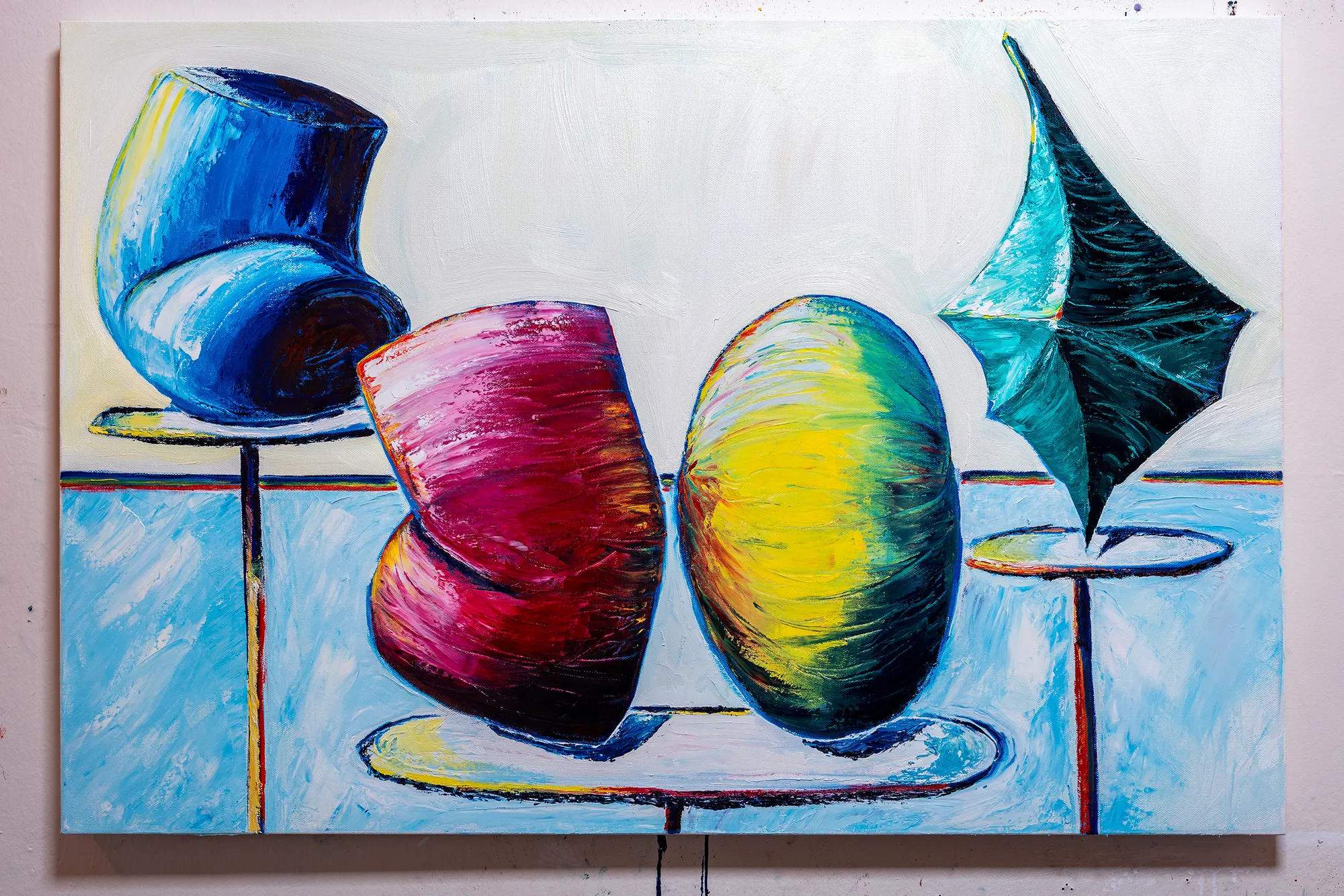 Display Room on a studio wall: a tipped blue vessel, a magenta form and a yellow-green ovoid on stands, and a dark teal shape like a folded umbrella, against pale blue and cream.