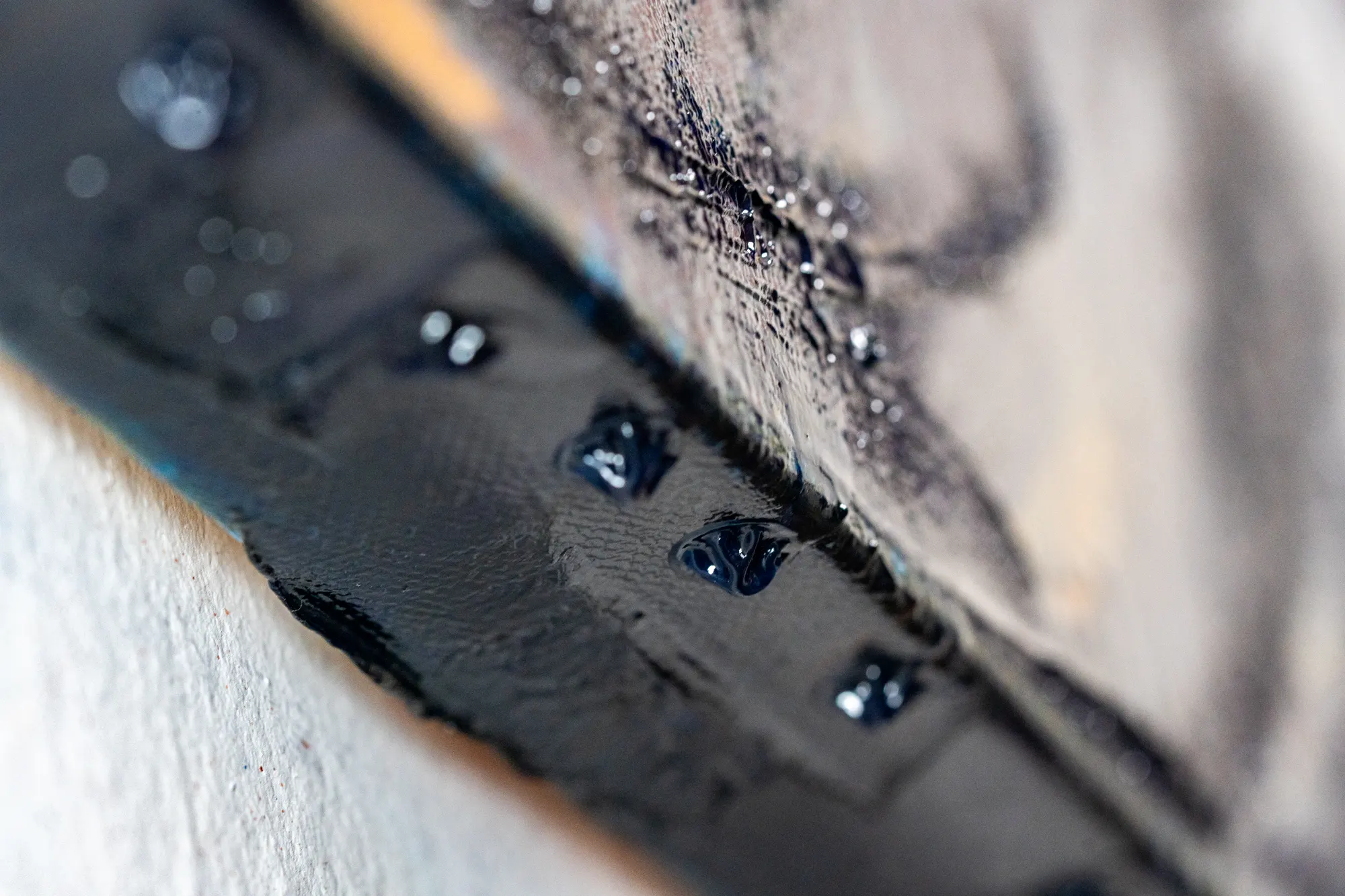 The bottom edge of the canvas, where beads of dark blue paint have gathered and hardened along the lip.