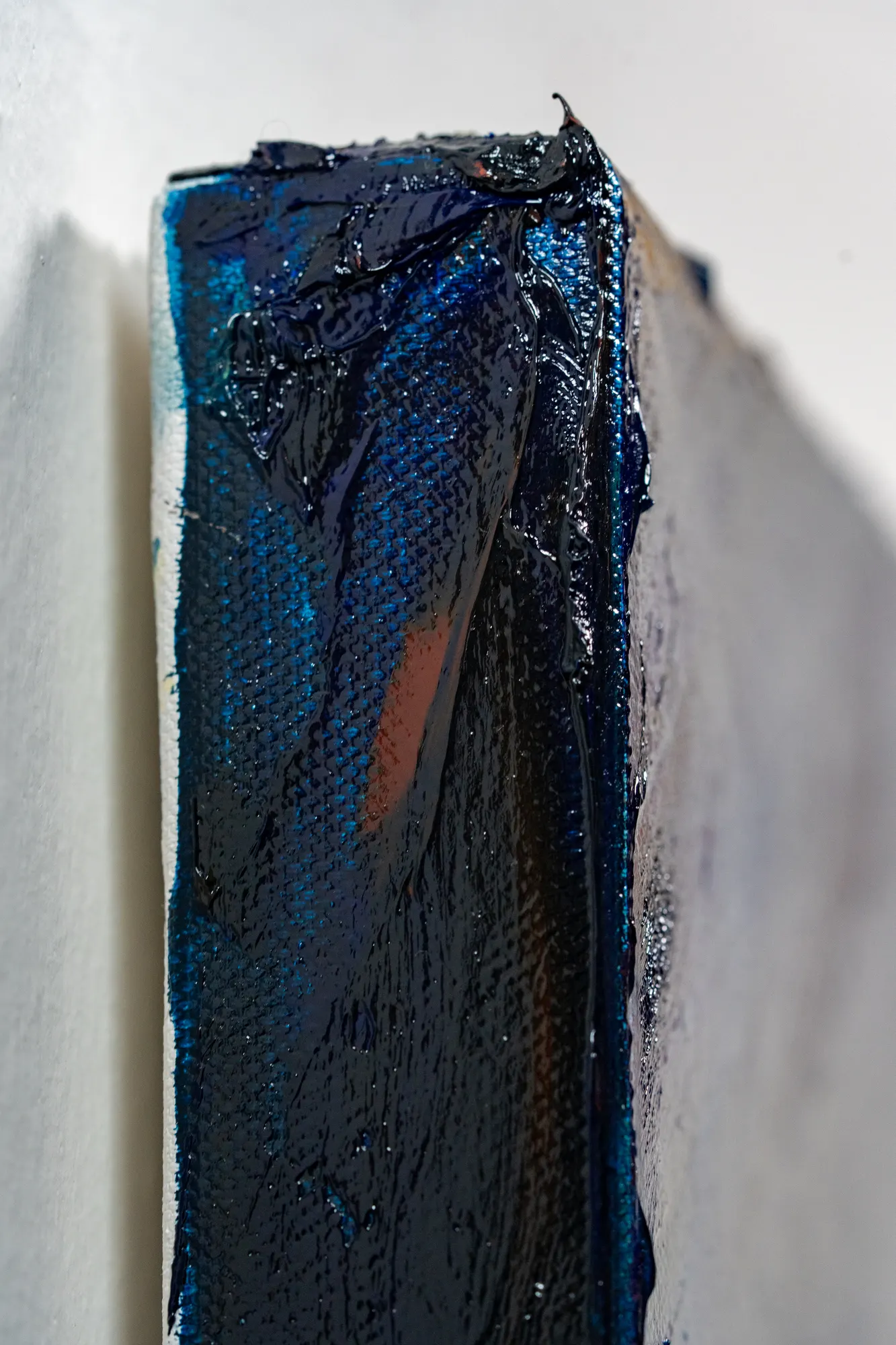 The canvas seen edge on, thick wet-looking blue paint wrapping around the stretcher bar.