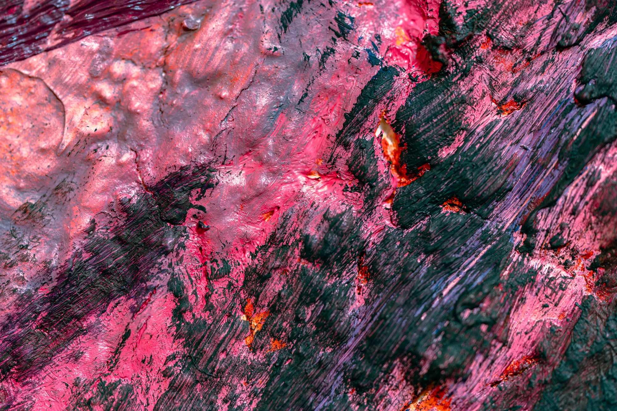 Close view of pink paint dragged across dark green and black, with orange caught in the gaps.