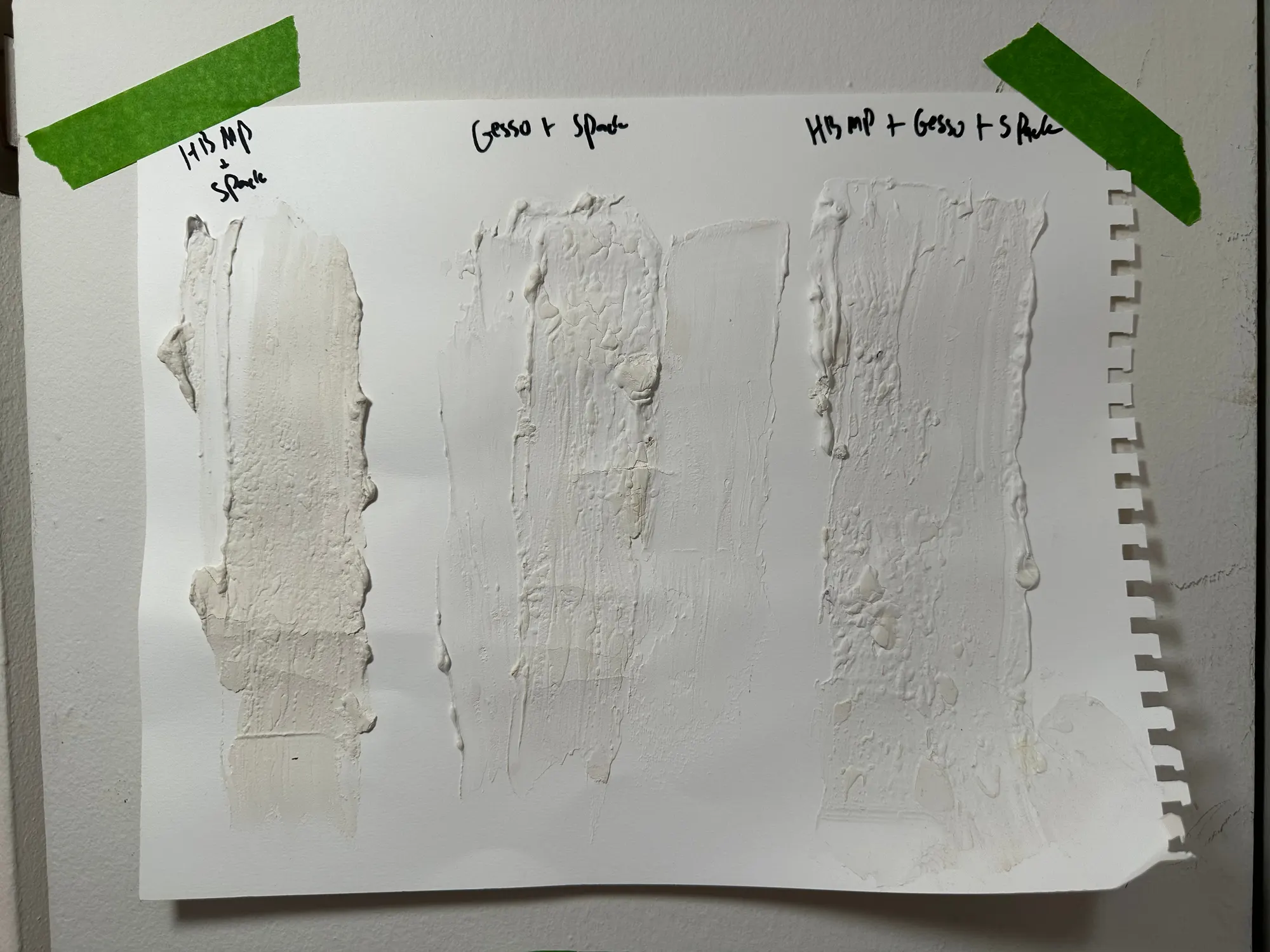 A sheet of paper carrying three thick white swatches labelled by hand: heavy body modeling paste with spackle, gesso with spackle, and all three combined. The middle swatch has dried with cracks running through it.