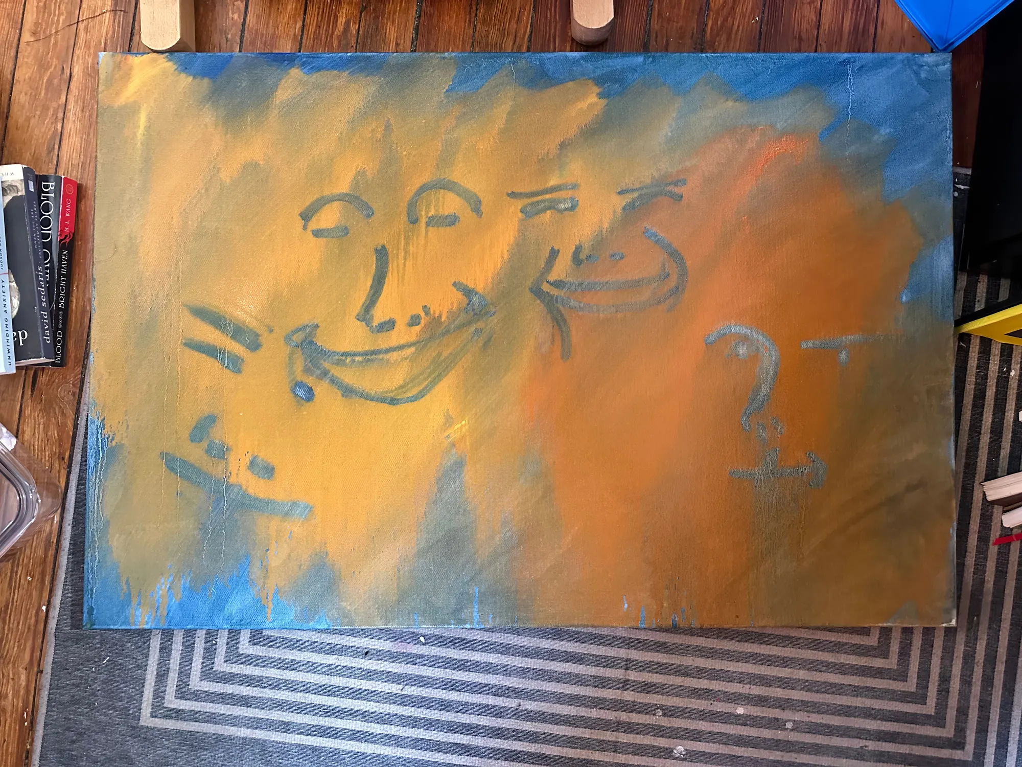 The first layer of Blue #1: thinned orange and ochre paint across the canvas with blue at the edges, and four caricature faces drawn into the wet paint in grey-blue.