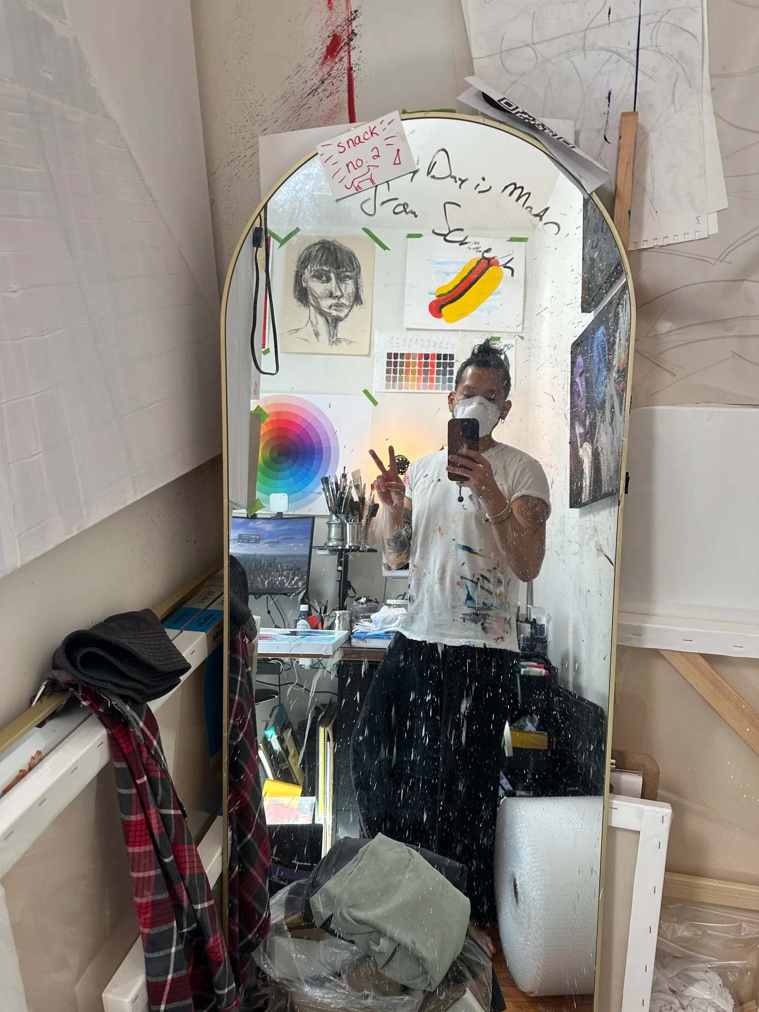 The artist in a full-length studio mirror wearing a respirator mask and a paint-covered shirt, surrounded by canvases and packing material on the final day of varnishing.